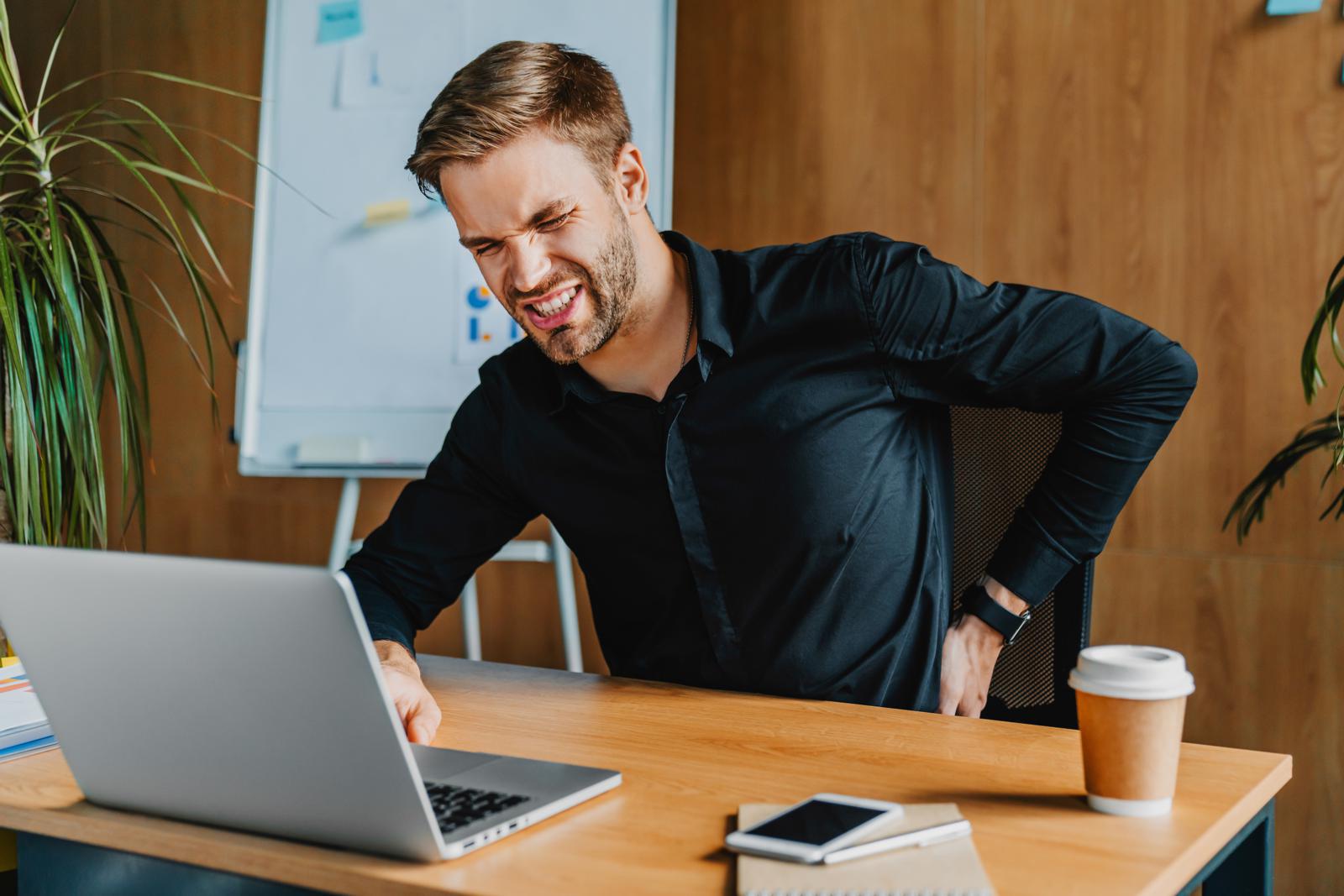 Businessman sitting at work desk with laptop having back pain in office